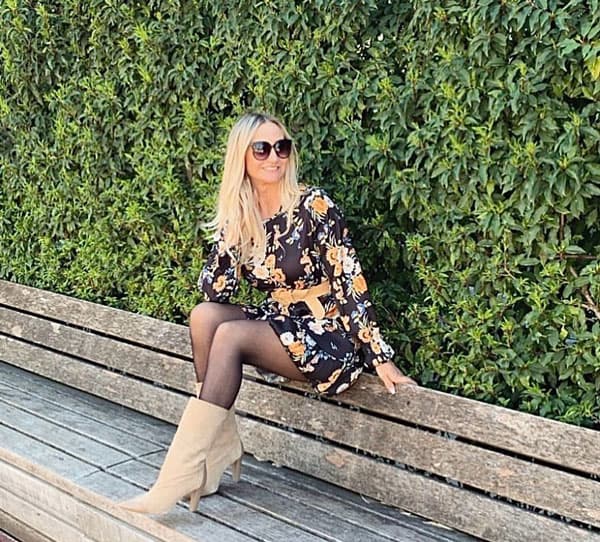 Marina Dojmi sitzt vor einer grünen Hecke auf einer Holzbank.